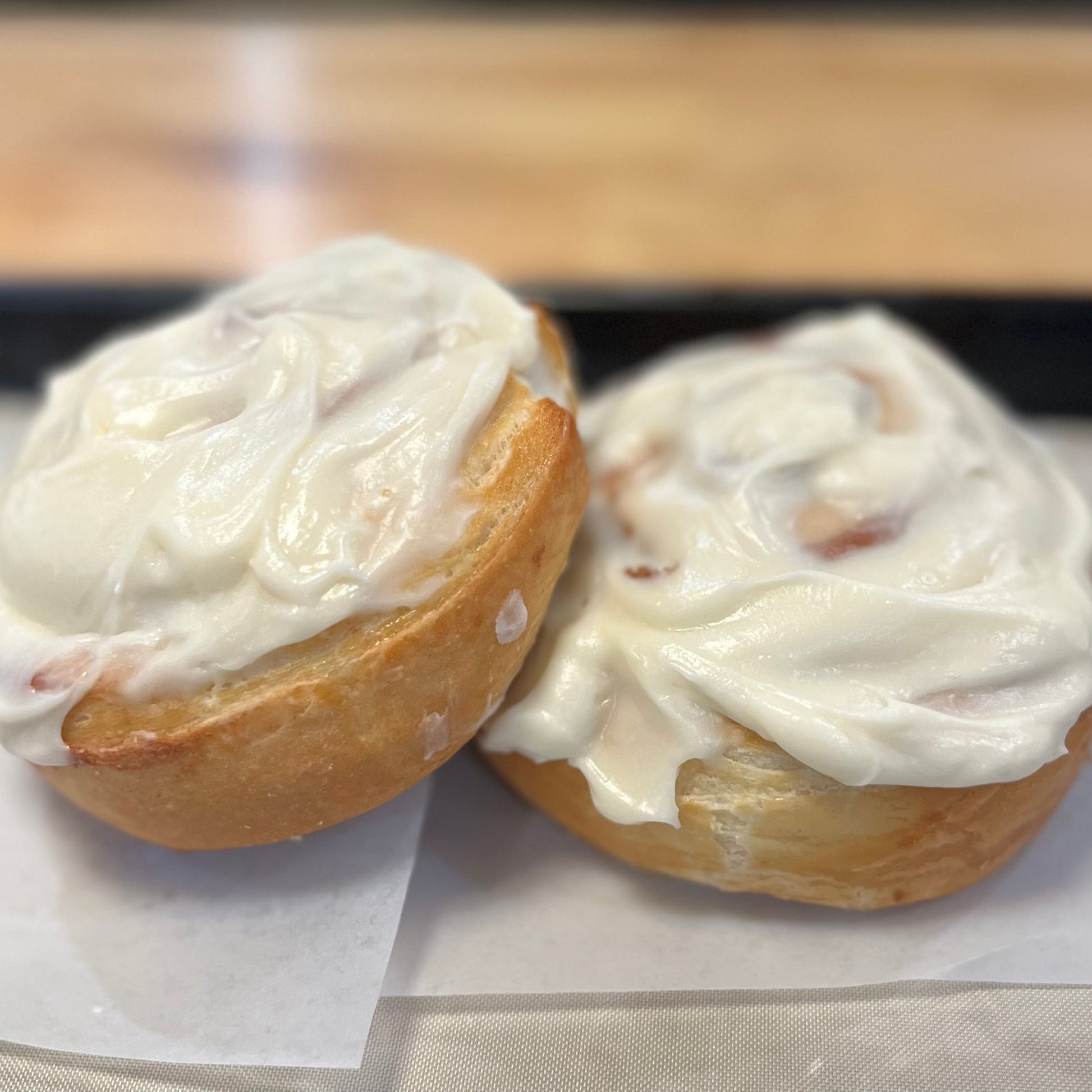 Two cinnamon rolls with white frosting on a white paper background
