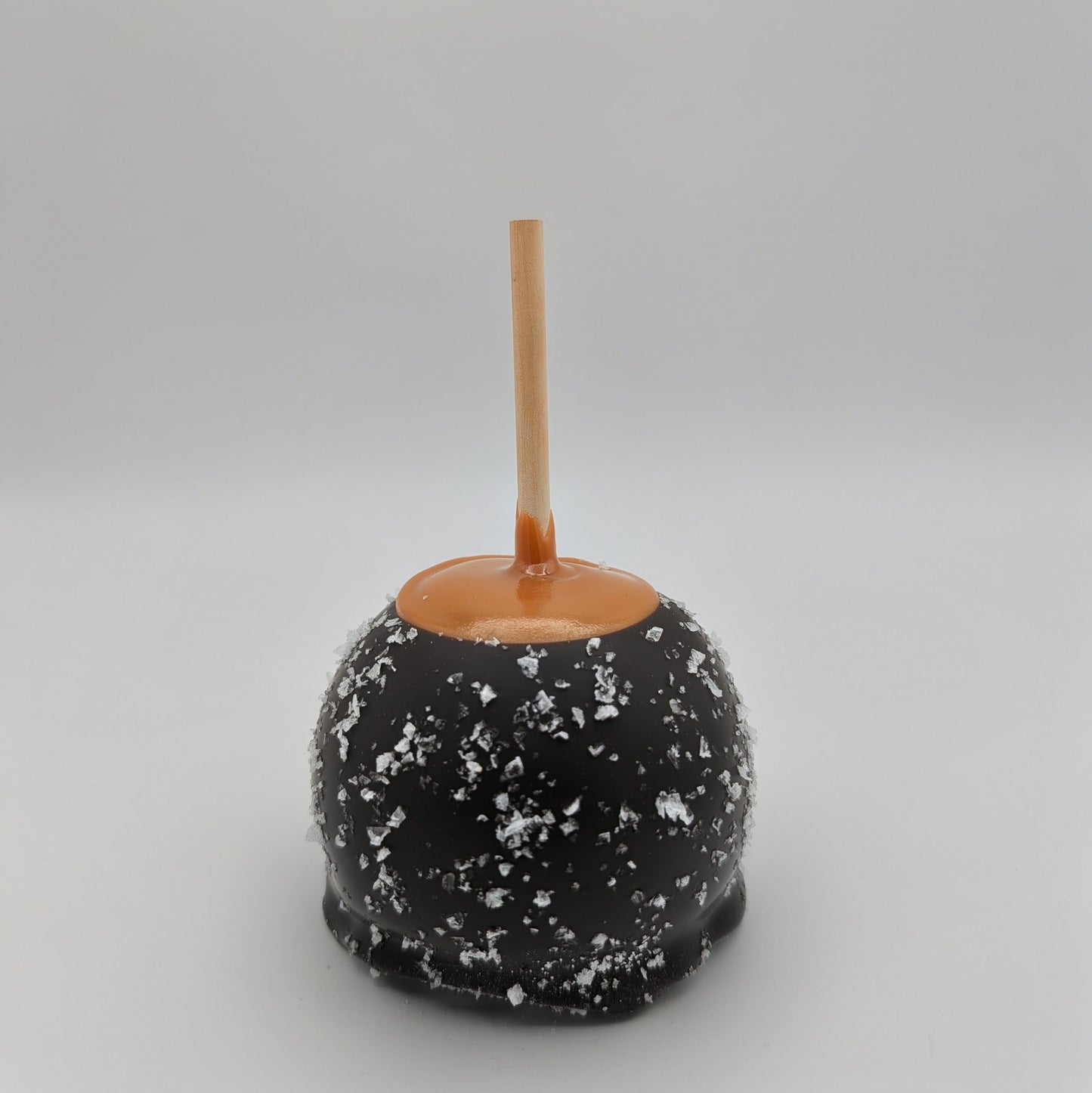 Caramel apple with dark chocolate ans sea salt coating on a gray background