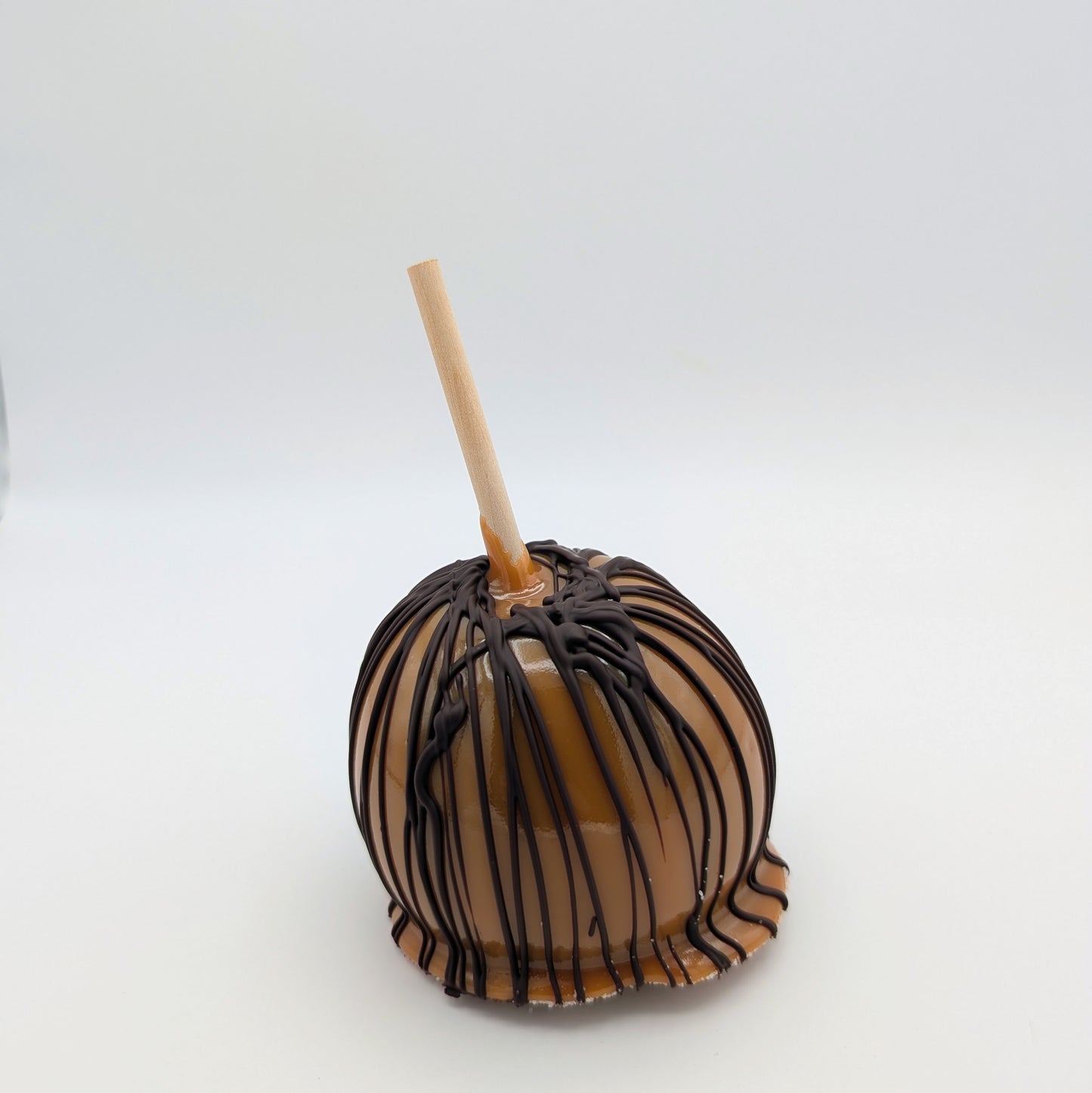 Chocolate caramel apple with a stick on a white background