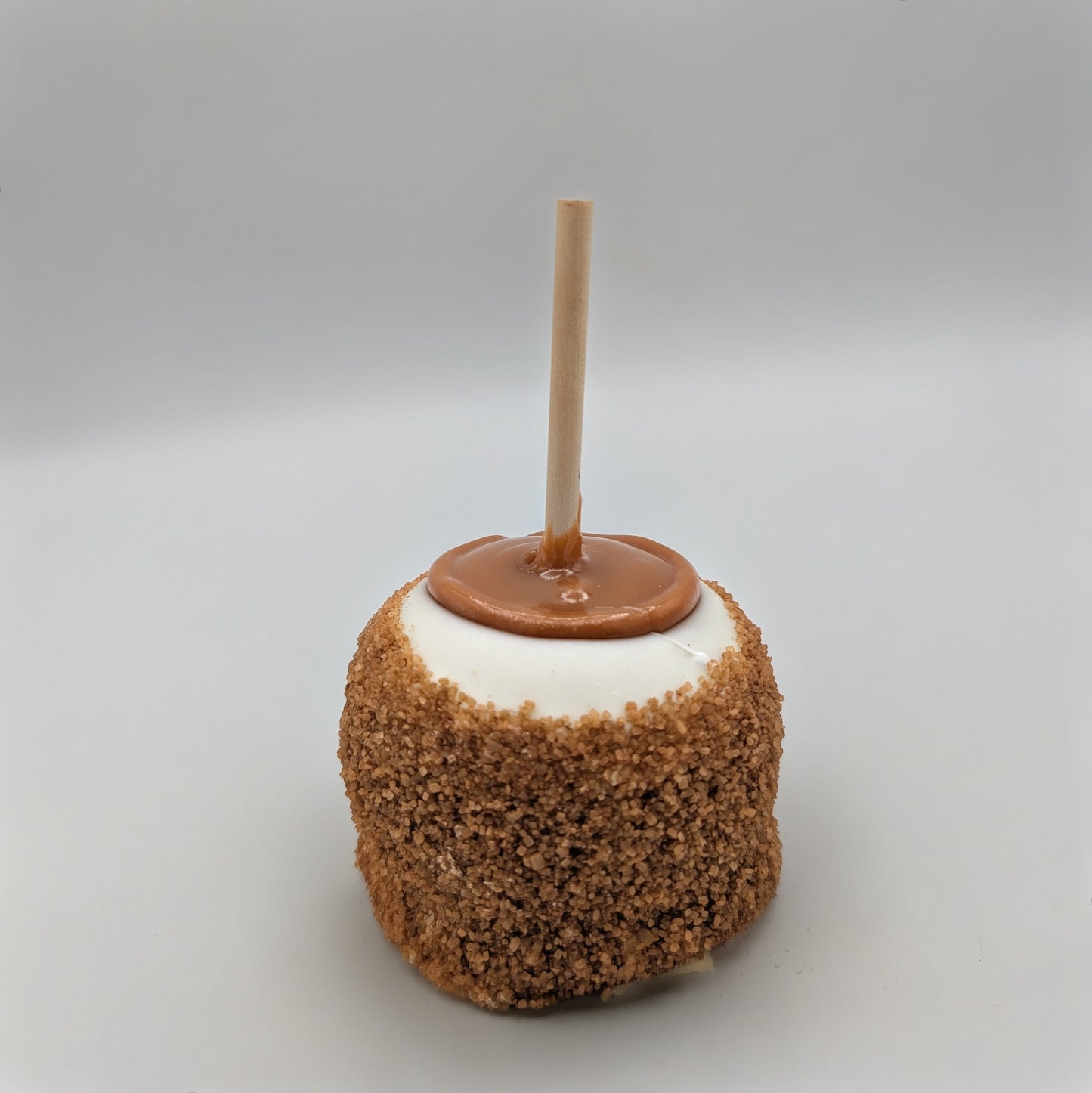 White chocolate covered caramel apple with a stick on a gray background. Apple pie apple. Cinnamon Sugar Apple