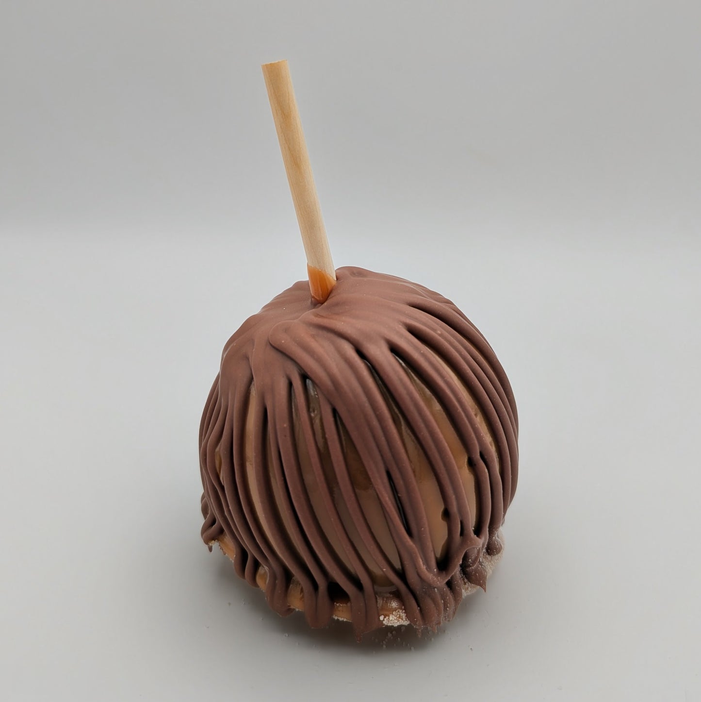 Chocolate caramel apple with a stick on a white background